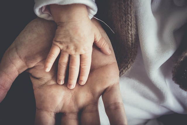 A surrogate mother holding hand of new born baby baby